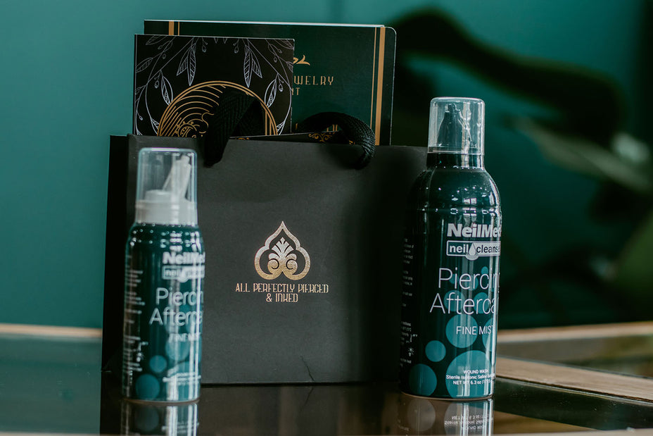 Sfeervolle presentatie van All Perfectly Pierced winkeltasje met reinigingssprays, focus op nazorg en stijlvolle verpakking.